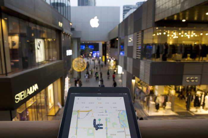 A mobile device displaying the Didi Chuxing app is posed near the Apple store logo in Beijing, China, Friday, May 13, 2016. Apple Inc. has invested $1 billion in Chinese ride-hailing service Didi Chuxing, the main competitor in China for Uber Technologies Ltd.